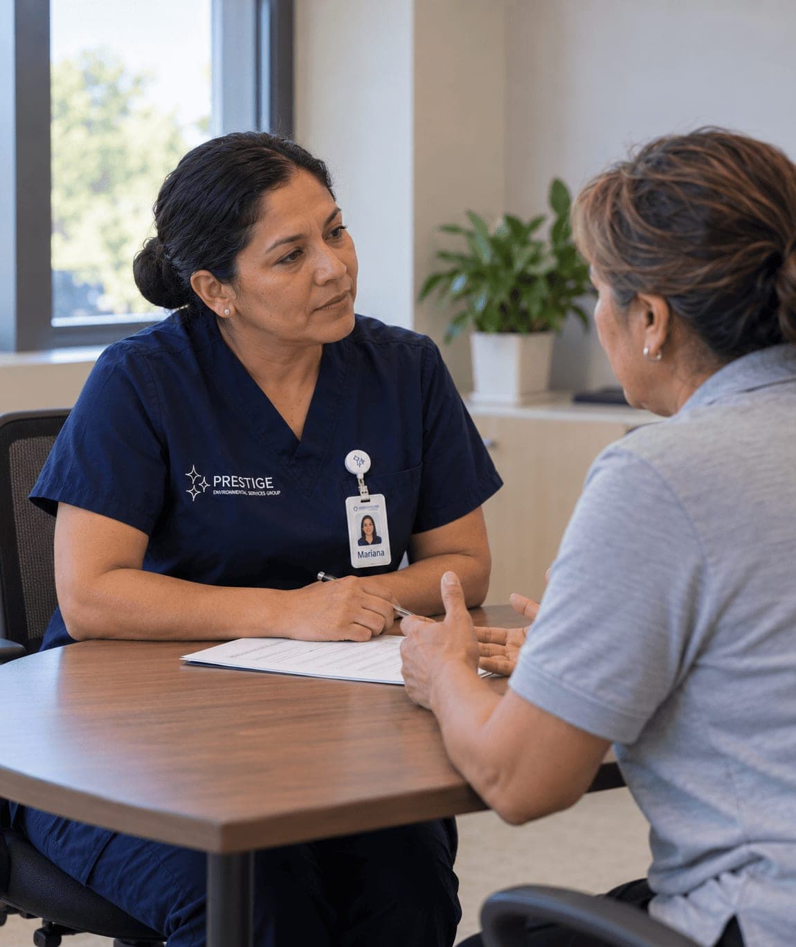 A Prestige housekeeping manager listening to a facility housekeeper across a table during a transition interview.